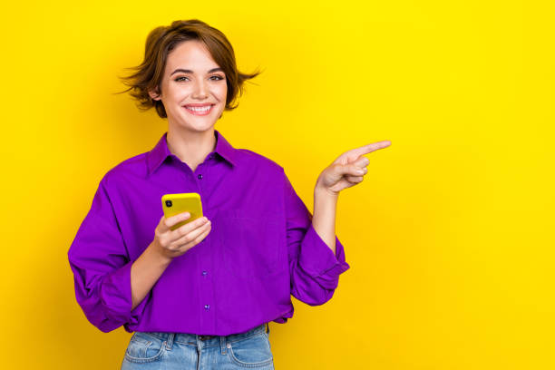 Photo of young satisfied businesswoman hair wear purple shirt direct finger fast speed wifi phone isolated on yellow color background stock photo