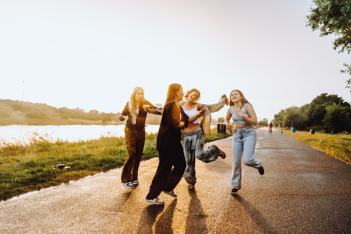 party young happy girls in nature. company young women, teenage girls, smiling, with hair wet from rain, having fun, taking selfies and dancing in nature by river, in rays of setting sun, glare lens