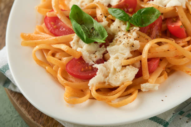 salat-caprese oder pasta-spaghetti gebrochen mit basilikum und mozzarella ala caprese auf weißem teller auf grünem rustikalem holzhintergrund. traditionelle italienische küche. italienisches food-konzept. draufsicht. rezept. - caprese salad antipasto wine mozzarella stock-fotos und bilder