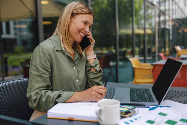 istock Smiling woman manager talking with client and work on laptop on cafe terrace. Distance work concept 1516753380