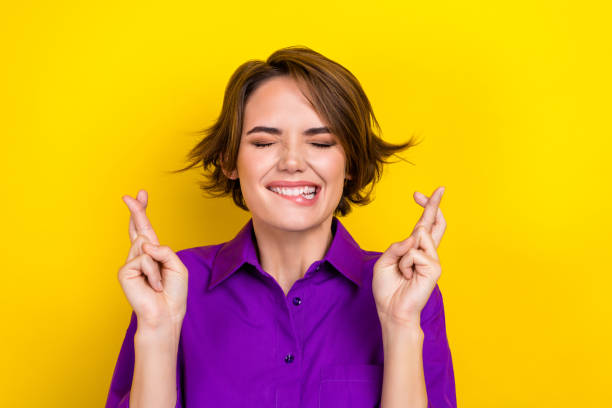 Photo portrait of pretty young girl cross fingers close eyes dressed stylish purple smart casual outfit isolated on yellow color background stock photo