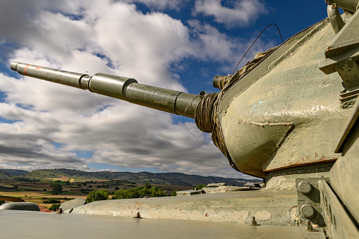 close-up of the cannon in the turret of a tank, armored car M60 patton, of the disabled Spanish army, green exposed in Rojas, a small town in Burgos, in the middle of the field on a mound, on the grass in the background the sky half blue half with clouds