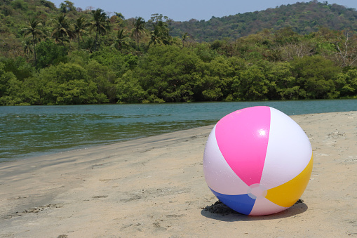 Stock photo showing sandy beach with a colourful, plastic beach ball children's beach toy left by water's edge.