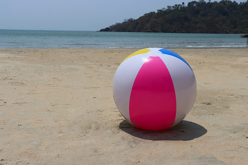 Stock photo showing sandy beach with a colourful, plastic beach ball children's beach toy left by water's edge.