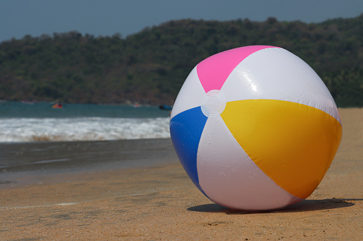 Stock photo showing sandy beach with a colourful, plastic beach ball children's beach toy left by water's edge.