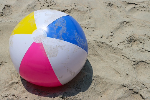 Stock photo showing elevated view of sandy beach with a colourful, plastic beach ball children's beach toy left by water's edge.
