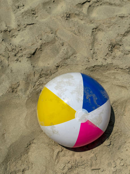 Stock photo showing elevated view of sandy beach with a colourful, plastic beach ball children's beach toy left by water's edge.