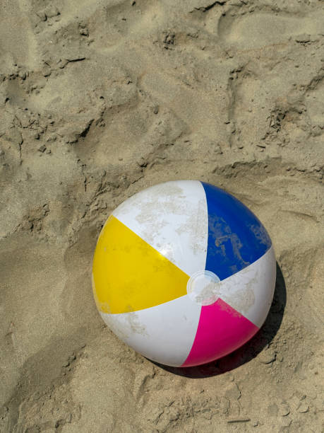 Image of plastic beach ball left on sandy beach at low tide, bright coloured children's beach toy, elevated view, copy space stock photo
