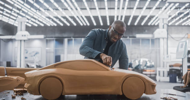 istock African Car Modeler Enjoying Creative Work Process on a Concept Car Made Out of Plasticine Modeling Clay. Handsome Black Designer Using Spatula to Smooth the Prototype Model of an Electric Vehicle 1516862049