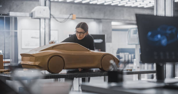 istock Automotive Designer Using 3D Software on Computer. Close Up on Screen Out of Focus and Female Modeler Creating a Clay Model of the Car. Team of Young Specialists Working in a Product Design Agency 1516864396