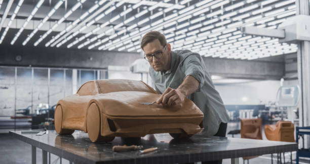 istock Car Modeler Enjoying Creative Work Process on a Concept Car Made Out of Plasticine Modeling Clay. Handsome Designer Using Spatula to Smooth the Sporty Prototype Model of a Modern Electric Vehicle 1516866925