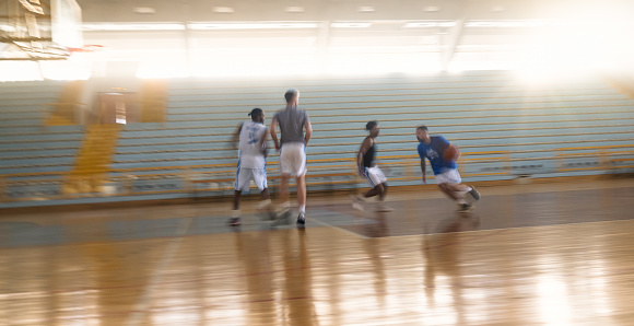 A group of professional basketball players training on an indoor court. They are in two groups and playing basketball game. Blurred motion photo. Concept of team sport and healthy lifestyle.