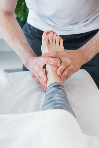 Caucasian woman being treated by therapist to relieve pain or improve physical condition. Therapist doing pressure and massage exercises through the feet to improve the overall health of the patient.