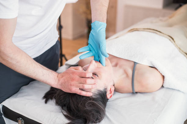 terapista osteopatico che fa trattamento a donna caucasica con problema alla mascella, allineamento mandibolare. trattamento per alleviare il dolore e migliorare le condizioni di salute del paziente. - osteopath chiropractic adjustment skull massaging foto e immagini stock