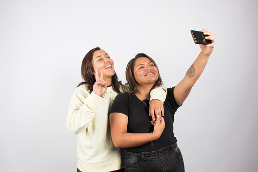 photograph of a female couple taking a selfie on a light studio background. Concept of people and human relationships.