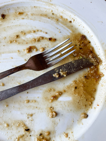 Stock photo showing close-up, elevated view of dirty white plate with the gravy remains of a Sunday Roast Dinner. Almost clean plate, as everything has been eaten with metal knife and fork.