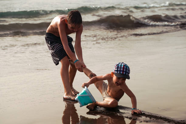 istock Boy pulling a brother during the game on the beach. Children have fun playing on the ocean. A fun summer vacation. Happy family. 1516967938