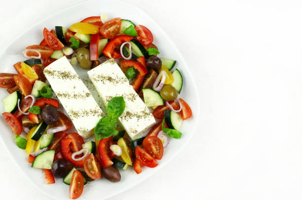 Concept of greek cuisine. Plate with fresh vegetables salad and feta cheese isolated on white background. Overhead view.