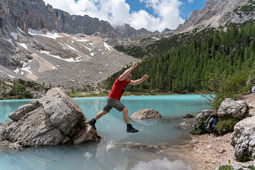 Side-view of Caucasian man jumping from rock to the shore of Lake Sorapis