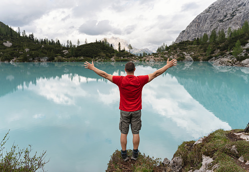 Rear view of unrecognizable Caucasian man admiring the beauty of the turquoise-colored Sorapis Lake, with arms raised