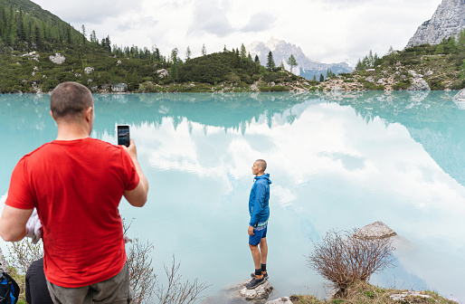 Caucasian man with mobile phone, taking photos of his friend near the turquoise-colored Sorapis Lake