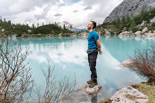 Caucasian man admiring the beauty of the turquoise-colored Sorapis Lake, while standing on a rock