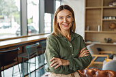 Female entrepreneur standing with crossed hands on coworking space background and looking camera