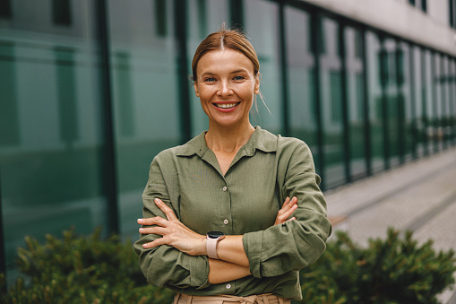 Smiling woman office worker is standing on modern building background and looking at camera