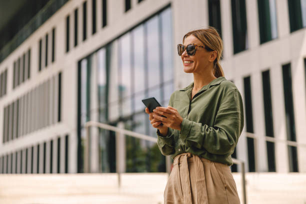 istock Woman freelancer in sunglasses using phone whiile standing on modern building background 1517038504