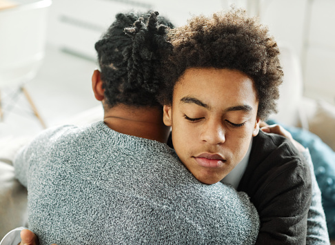 Portrait of son hugging his father, together at home. Son caring for his father, putting hand on his shoulder, comforting and consoling him. Family love, bonding, care and confidence