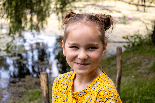 Lovely small girl sitting on a bench in the park and smiling at camera. High quality photo