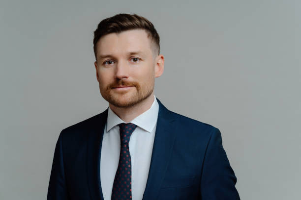 istock Young successful bearded businessman in suit, confident CEO, headshot posing, grey studio background. 1517123229