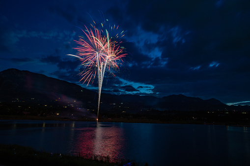 Fireworks reflections at Colorado Springs lake with Pikes Peak mountain range background and suburban lights in western USA of North America. Celebration of United States Independence Day, July 4.