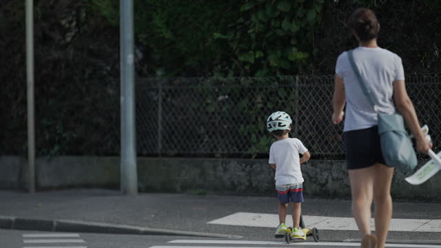 Child crossing street with scooter wearing protective helmet. Mother and kid at crosswalk zebra lines