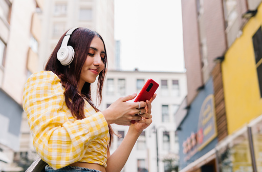 Low angle view photo of a woman listening to music with headphones and the mobile phone in the street