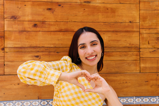 Happy beauty woman representing a heart in the shape with hands standing and looking at camera