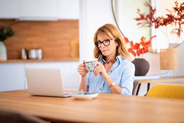 istock Mid aged woman with earphone, using laptop and having video call at home 1517185087