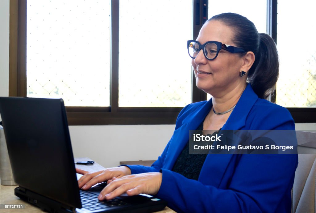 Woman with ponytail hair wearing eyeglasses sitting and working comfortably at table with laptop Scene with home office work style, with woman over 50 years old 45-49 Years Stock Photo