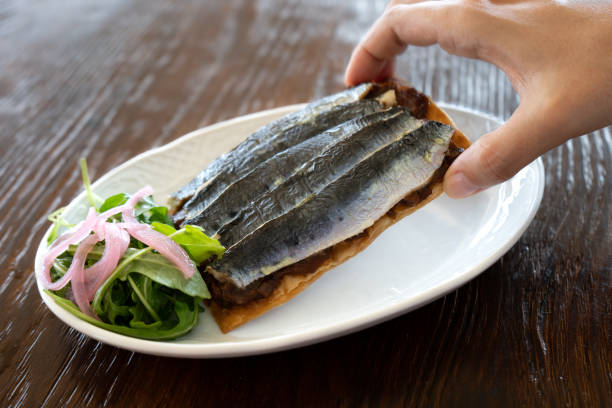 gros plan de la main d’une femme prenant un toast à la sardine de style gastronomique dans l’assiette - gourmet salad dinner prepared fish photos et images de collection