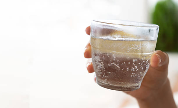 Close-up of a woman's hand holding a glass of cold sparkling water with a squeeze of lemon with copyspace on the side stock photo