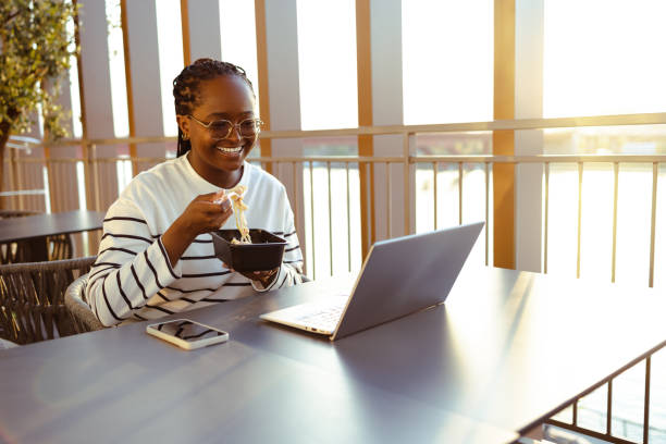 jeune femme souriante utilisant un ordinateur portable pendant la pause déjeuner - box lunch flash photos et images de collection