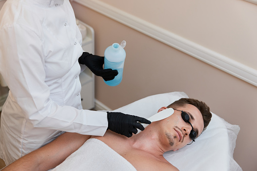 beautician applies cooling gel to male facefor receiving epilation in beauty center.
