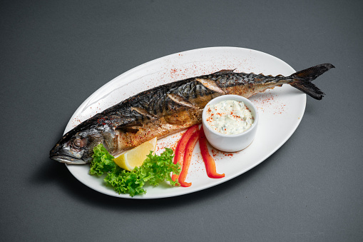 grilled mackerel fish with lemon and sauce on white plate on dark background