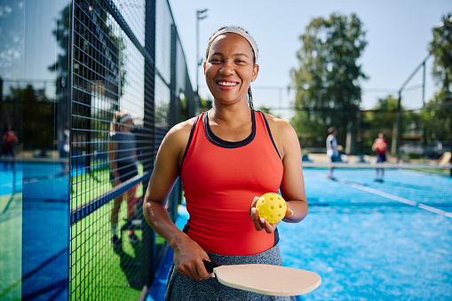 Happy African American woman playing pickleball on an outdoor court and looking at camera. Copy space.