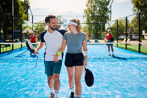 Happy athletic couple having fun while playing padel tennis doubles match on outdoor court.