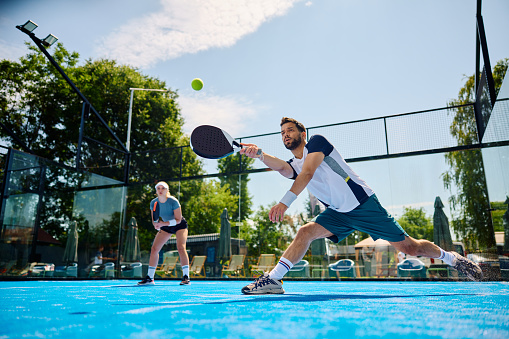 Young athlete playing padel in mixed doubles on outdoor court. Copy space.