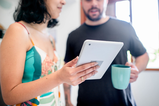 Close-up of young couple with coffee using digital tablet standing together at home