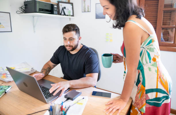 istock Young man working on laptop with his girlfriend holding coffee at home 1517507604