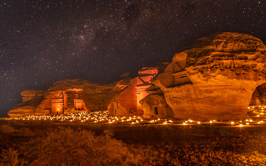 Starlight sky over the ancient nabataean tombs of Hegra city illuminated, night panorama, Al Ula, Saudi Arabia