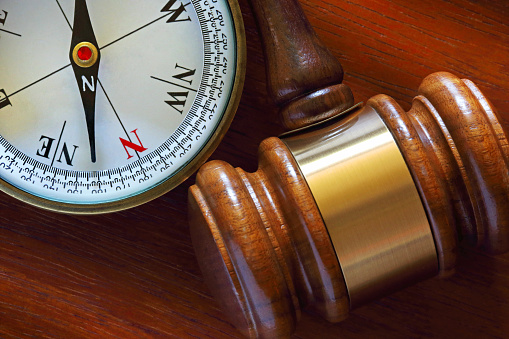 A compass sit next to a gavel on a wood desk.